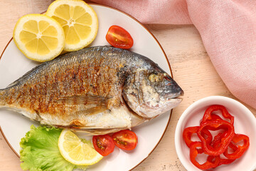 Plate with tasty grilled dorado fish on light wooden background