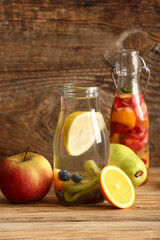 Bottles of infused water with different sliced fruits on wooden table