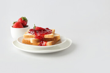 Plates and tasty toasts with strawberry jam on white background
