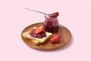 Wooden plate of tasty toasts with strawberry jam and spoon on pink background