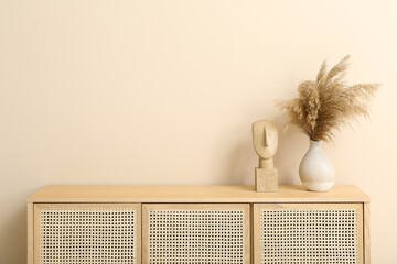 Wooden chest of drawers with pampas grass and decor near beige wall in room