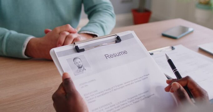 Close-up of an African American hr manager hands holding a resume during meeting or interview with new employee in office. Discussion, teamwork, partnership, recruitment, and company collaboration.