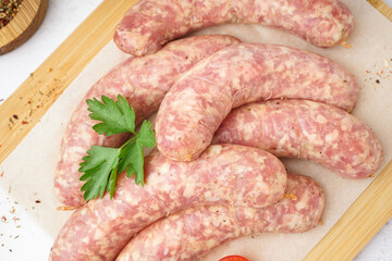 Wooden board with raw homemade sausages on light background