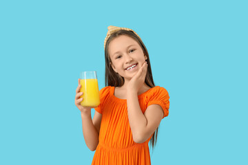 Obraz premium Cute little girl with glass of orange juice on blue background