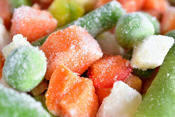 Pieces of frozen vegetables such as carrots, green beans, peas, zucchini. Close-up.