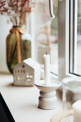 Candle and decorative house on the windowsill at home.