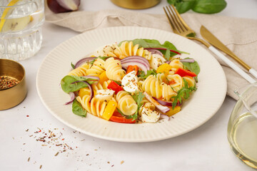 Plate of tasty pasta salad with pepper and red onion on white background