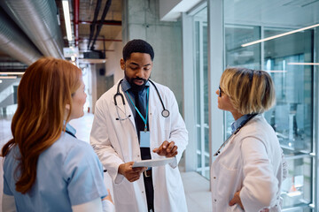 Black doctor using touchpad during meeting with female colleagues in hospital.