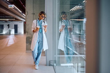 Female doctor using cell phone on coffee break at hospital.