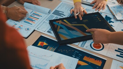 A diverse business team engages in collaborative work, analyzing charts and reports while using a digital tablet to drive strategic decisions in a modern office setting. SACTR