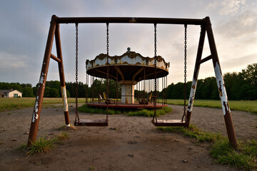 Abandoned Playground with a Weathered Carousel and Swings Against a Cloudy Sky, Evoking Nostalgia and Forgotten Memories