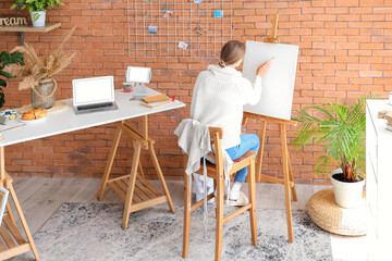 Female artist painting on easel in studio, back view
