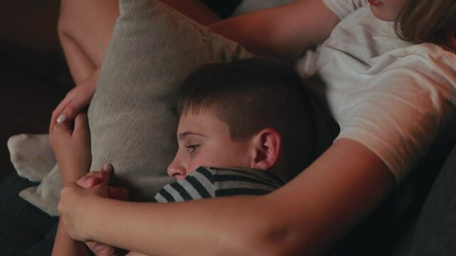 Sensitive moment capturing young siblings' emotional connection, with caring sister providing comfort and support while hugging and holding hands with her distressed brother on family sofa