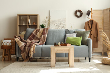 Interior of modern living room with grey sofa, warm blanket and pine cones on coffee table