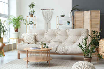 Interior of light stylish living room with sofa, table, houseplants, shelving unit and window