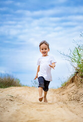 Child running joyfully on sandy path. A young child is happily running barefoot along a sandy trail...
