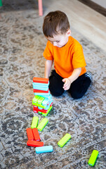 Fototapeta premium Child stacking colorful blocks on carpet. A child in an orange shirt stacks colorful blocks on a patterned carpet, displaying creativity.