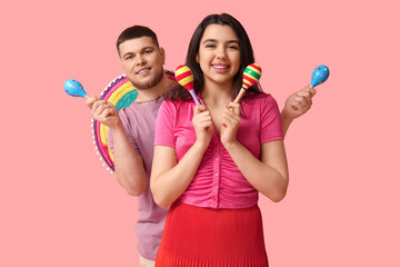 Beautiful young happy couple with sombrero and maracas on pink background. Cinco de Mayo celebration
