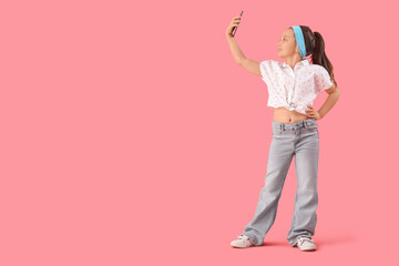 Naklejka premium Portrait of fashionable little girl taking selfie on pink background