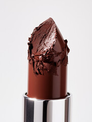 Close-up of a brown lipstick with a damaged tip. Rich, glossy finish and a slightly uneven texture due to the smudged surface. This image is perfect for use in beauty project