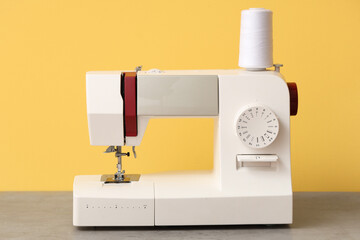 Modern sewing machine with thread spool on yellow background