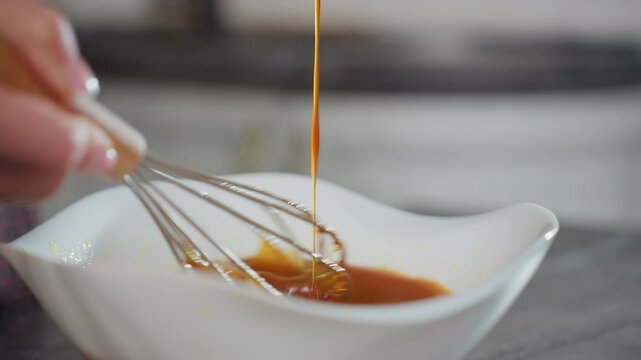 Close-up of person pouring rich red soup into white bowl while stirring with whisk, vibrant liquid flows smoothly as ingredients blend, creating a flavorful mixture in a modern kitchen