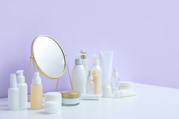 Different cosmetic products with mirror on table near lilac background