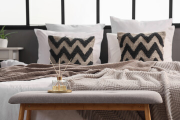 Grey bedside bench with reed diffuser near bed in modern bedroom, closeup