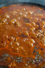 Boiling stew with bubbling tomato-based sauce, herbs, and spices in a pan, releasing steam and rich aroma
