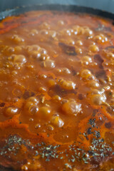 Boiling stew with bubbling tomato-based sauce, herbs, and spices in a pan, releasing steam and rich aroma
