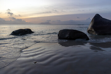 A peaceful beach scene featuring smooth sand, large scattered rocks