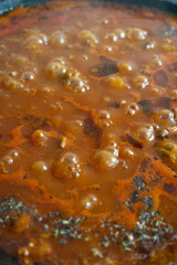 Boiling stew with bubbling tomato-based sauce, herbs, and spices in a pan, releasing steam and rich aroma