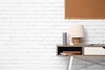 Lamp with burning candles on table near white brick wall in room