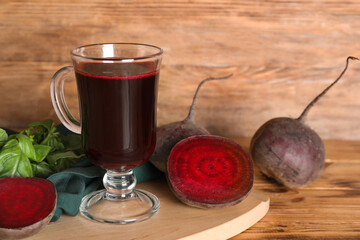 Glass of fresh beet juice with basil and vegetables on wooden background