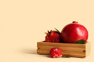 Wooden box with fresh ripe pomegranates and leaves on yellow background