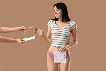Young woman in menstrual panties and hands holding tampon with pad on beige background