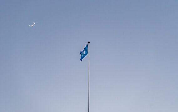 United Nations flag under crescent moon and Venus at dusk