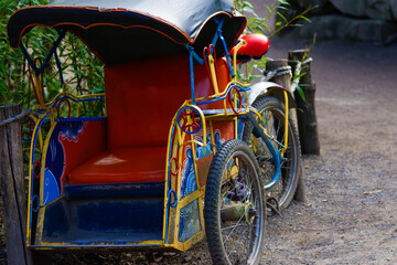 Colorful rickshaw with intricate designs parked on a dirt path.