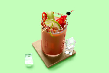 Glass of bloody mary cocktail with chili pepper, celery and ice cubes on green background