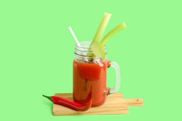 Mason jar of bloody mary cocktail with chili pepper, celery and lime on green background
