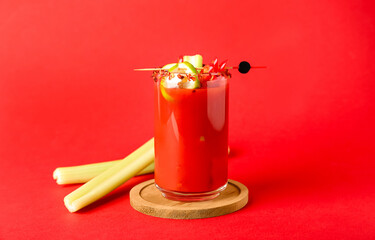 Glass of bloody mary cocktail with chili pepper and celery on red background