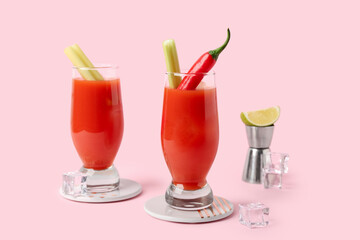 Glasses of bloody mary cocktail with chili pepper and celery on pink background