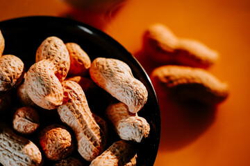 Peanuts in a black bowl against a warm orange background creating a cozy snack setting