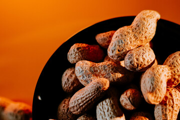 Peanuts stacked in a black bowl with warm orange background create a cozy and inviting atmosphere at snack time