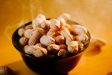Hot roasted peanuts in a black bowl with steam rising against a golden background