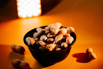 Nuts displayed in a black bowl illuminated by warm light on a vibrant yellow surface