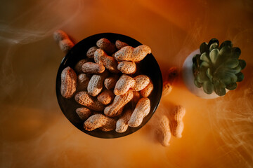 Peanuts in a black bowl with a succulent plant on a wooden table during cozy indoor setting