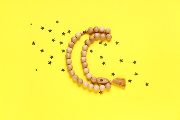Composition with crescent made of prayer beads and golden stars on yellow background. Ramadan celebration