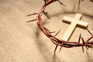 Crown of thorns with wooden cross on sand background