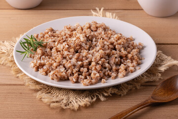 Cooked buckwheat served on a white plate with fresh herbs on a rustic wooden table